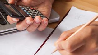 White hands holding a pencil and a calculator over paper on a desk